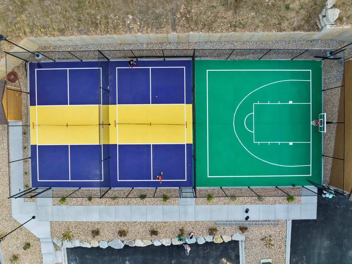 An inviting shot of the resort's outdoor tennis and basketball courts, with players engaged in games. The courts are surrounded by greenery, capturing the energy and communal spirit of on-site recreational opportunities.