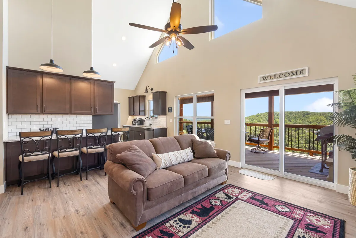 A stylish and inviting living area flows into a modern kitchen and dining space, all bathed in sunlight from large windows. The scene includes a comfortable sofa, kitchen island, and a table set for a meal, suggesting opportunities for relaxation and shared experiences.