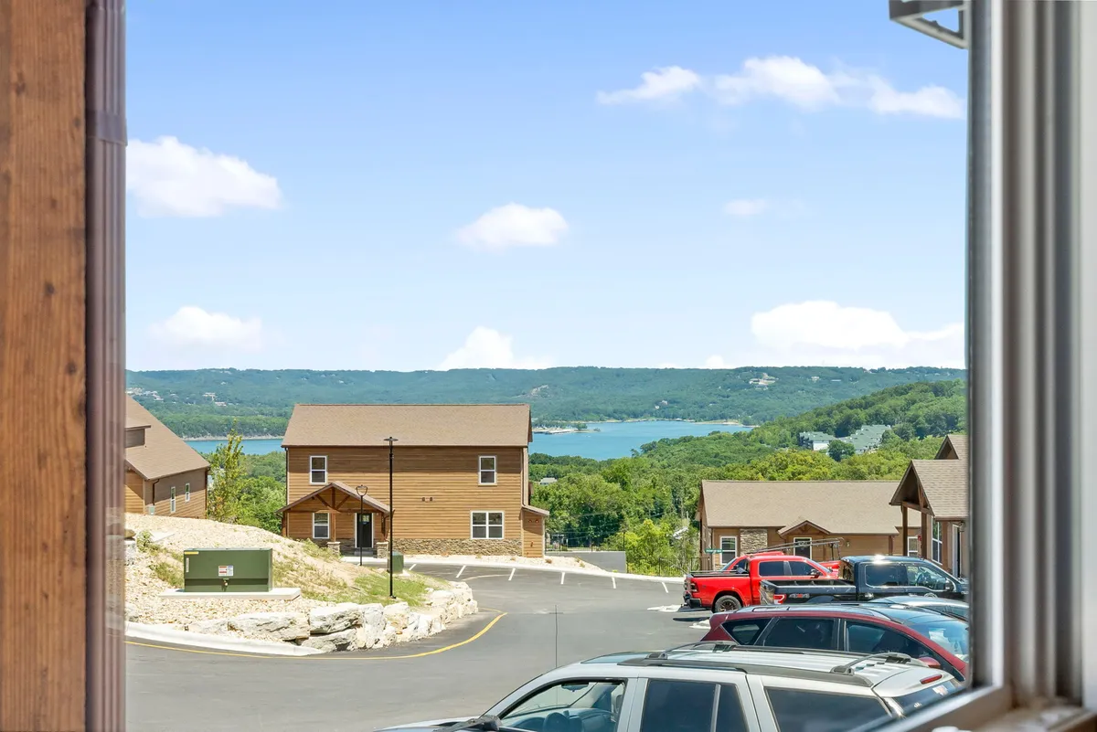 The scene showcases a picturesque lake view framed by wooden cabins and a small parking area in the foreground. It conveys a sense of calm and connection to nature, with ample open space for walks and outdoor activities. This setting visually demonstrates the property's proximity to nature and the opportunities for scenic exploration with pets.