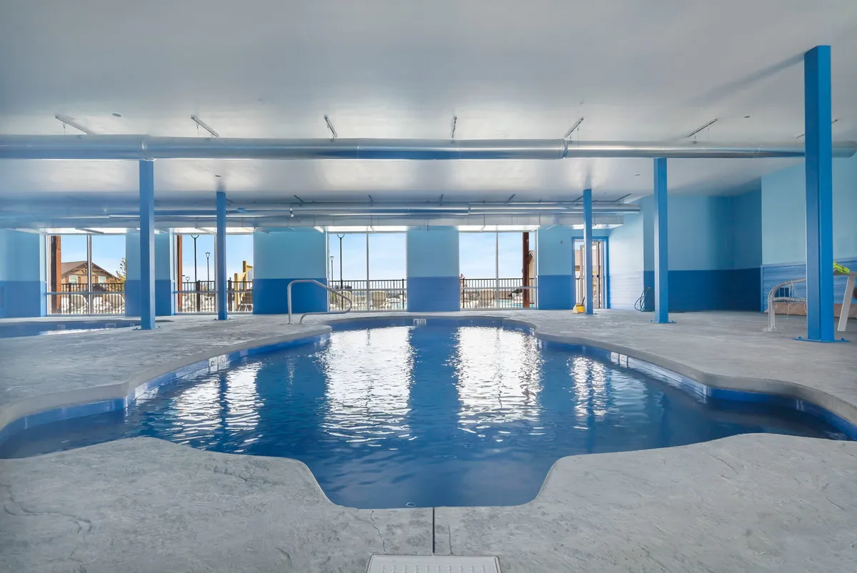 This image showcases a serene indoor swimming pool surrounded by large windows and blue-toned walls. The tranquil atmosphere is punctuated by the soft natural light streaming in, creating a year-round space for relaxation and activity.