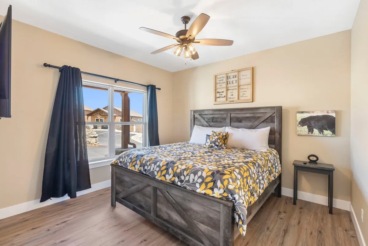 A serene bedroom with a large bed adorned in floral bedding, a wooden nightstand, soft curtains, and a large window letting in gentle daylight. Subtle wall art and inviting textiles create a warm, peaceful retreat ideal for couples or anyone seeking relaxation.