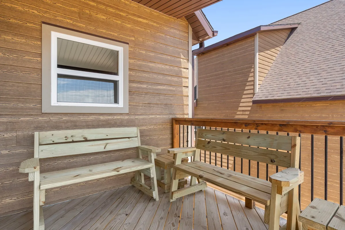A charming corner of the deck featuring wooden benches and a deck railing, positioned perfectly for quiet moments with views of the surrounding woods. The area is ideal for sipping coffee or enjoying the tranquil ambiance.