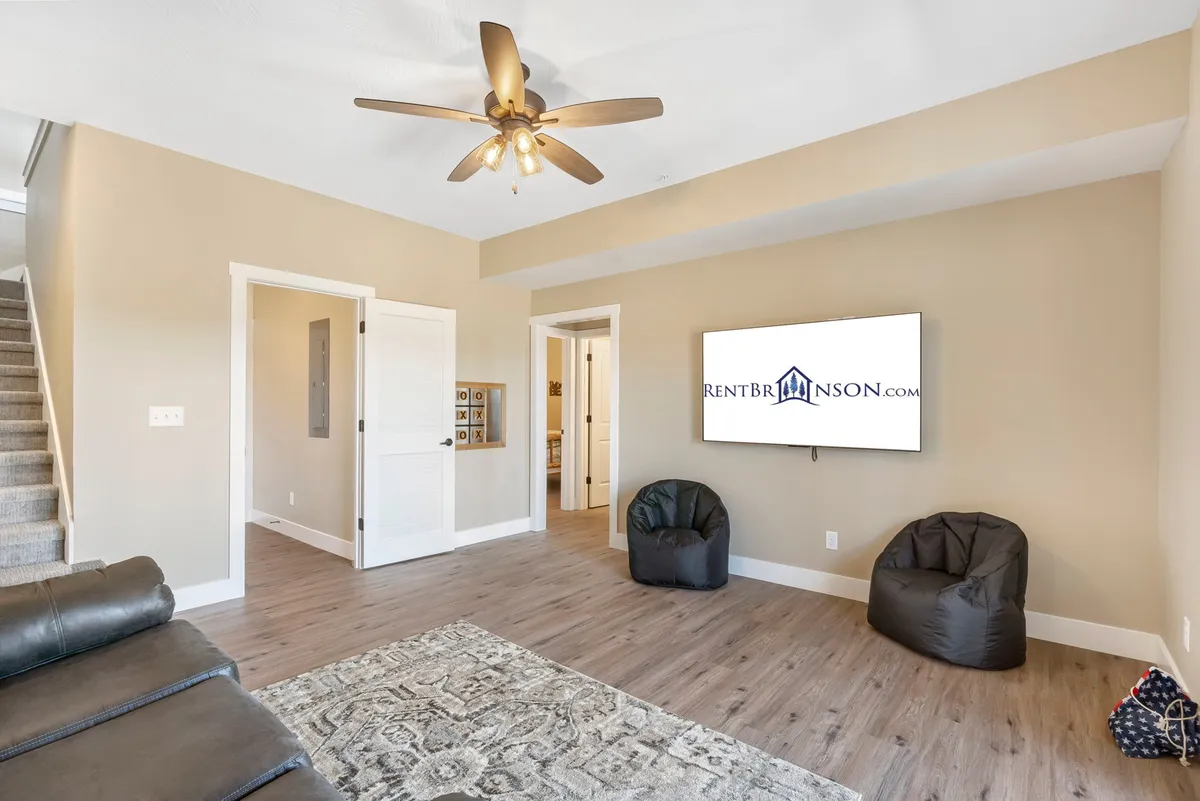 A casual and comfortable family room interior featuring bean bag chairs, a television, a ceiling fan, and an area rug. The relaxed setup is perfect for lounging, watching TV, or gathering for board games and group activities.