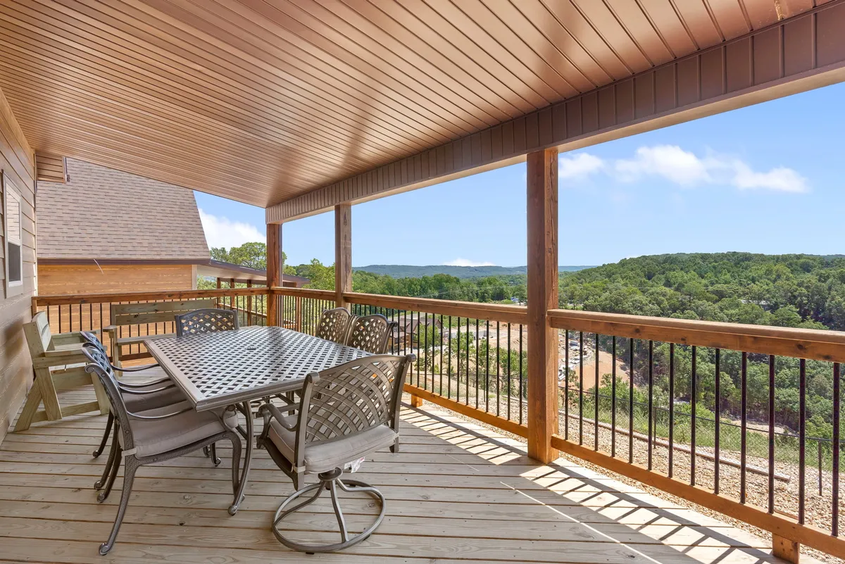 An inviting outdoor dining area on a wooden deck, with a large table and chairs surrounded by a serene forest backdrop. The scene is tranquil and set for a gathering, capturing the sense of space and connection to nature.