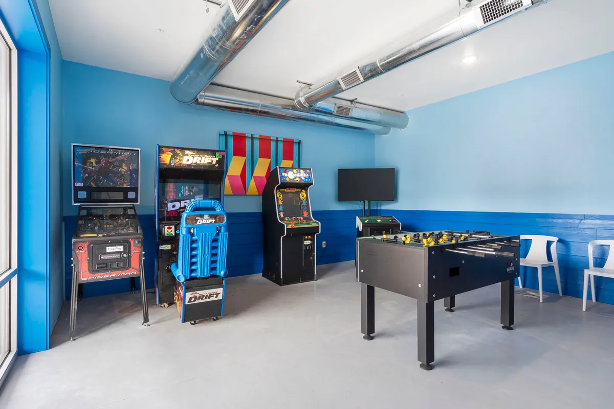 A bright and fun interior space with multiple arcade machines, a foosball table, and playful wall art. The layout encourages group gaming and socializing, evoking an atmosphere of excitement and energetic fun.